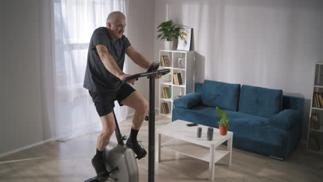 Hacer-Ejercicio-Con-Bicicleta-Estacionaria-En-Casa-Un-Hombre-De-Mediana-Edad-Está-Entrenando-Y-Girando-Pedales-Para-Mantenerse-En-Forma-Y-Hacer-Ejercicio-Cardiovascular-Saludable
